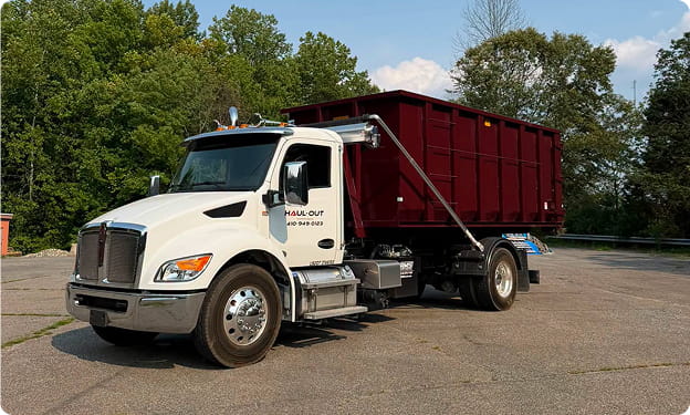Haul-Out roll-off dumpster truck carrying a red dumpster