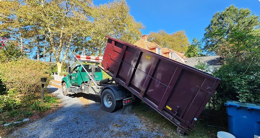 Green Haul-Out truck placing a roll-off dumpster at a residential property in Maryland